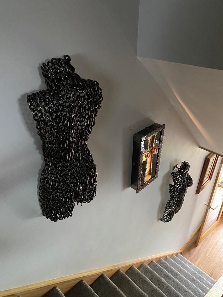 Metal torso wall sculpture beside framed artwork