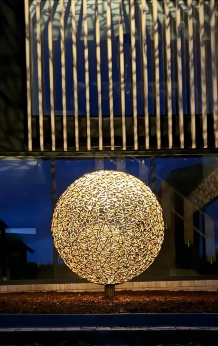 Illuminated lattice sphere and perforated steel light screen at dusk