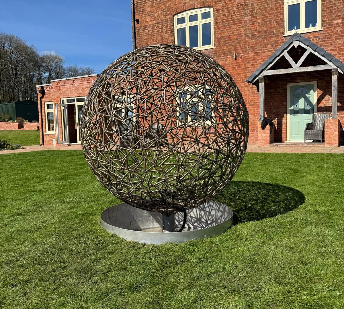 Lattice garden sphere on a lawn in front of a brick farmhouse